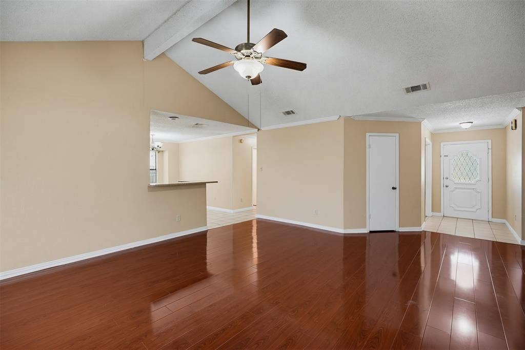 Vaulted ceilings, wood-finish flooring, ceiling fan with integrated lighting, pass-through opening, and decorative glass-panel entry door