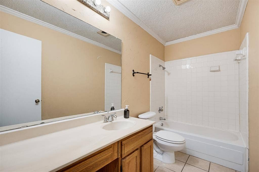 Bathroom featuring a wood-finish vanity with an integrated basin, a full-width wall mirror, a bathtub and shower combination with white tile surround, and tile flooring