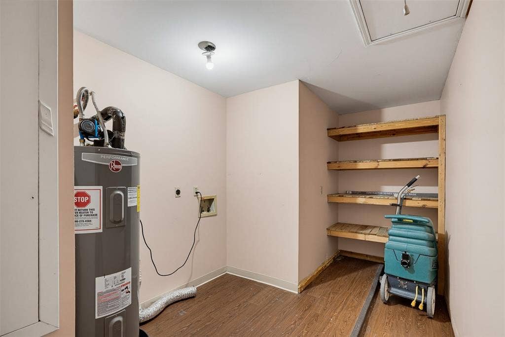 Utility area featuring wood-finish flooring, a water heater, and built-in wood shelving