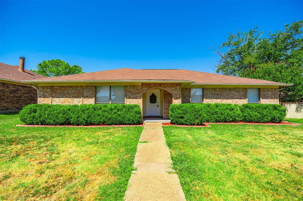 Single-story brick exterior featuring a shingled hip roof, arched entryway, and manicured shrubbery
