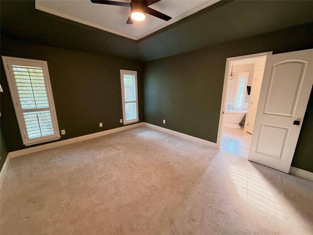 Tray ceiling with a central fan, neutral carpeting, and shuttered windows