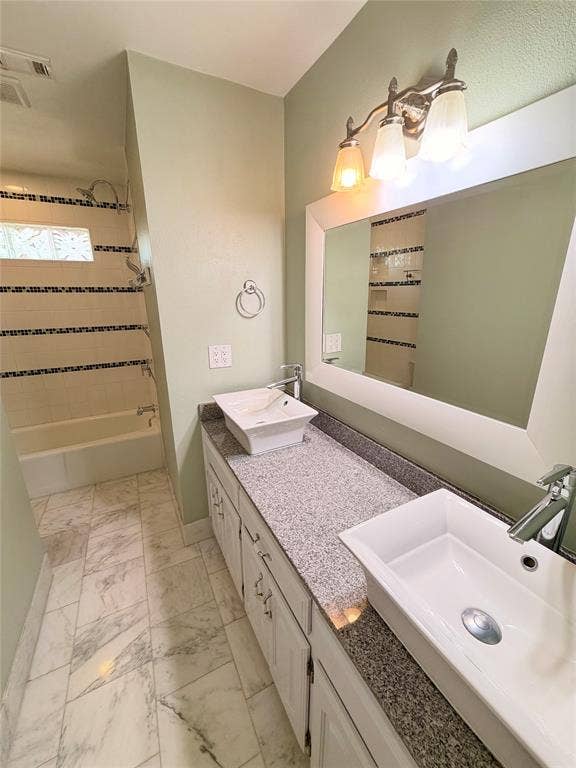 Double vanity featuring white rectangular vessel sinks, speckled stone countertops, and polished chrome faucets, complemented by white cabinetry, marble-style tiled flooring, and a shower-tub combination with decorative mosaic tile accents