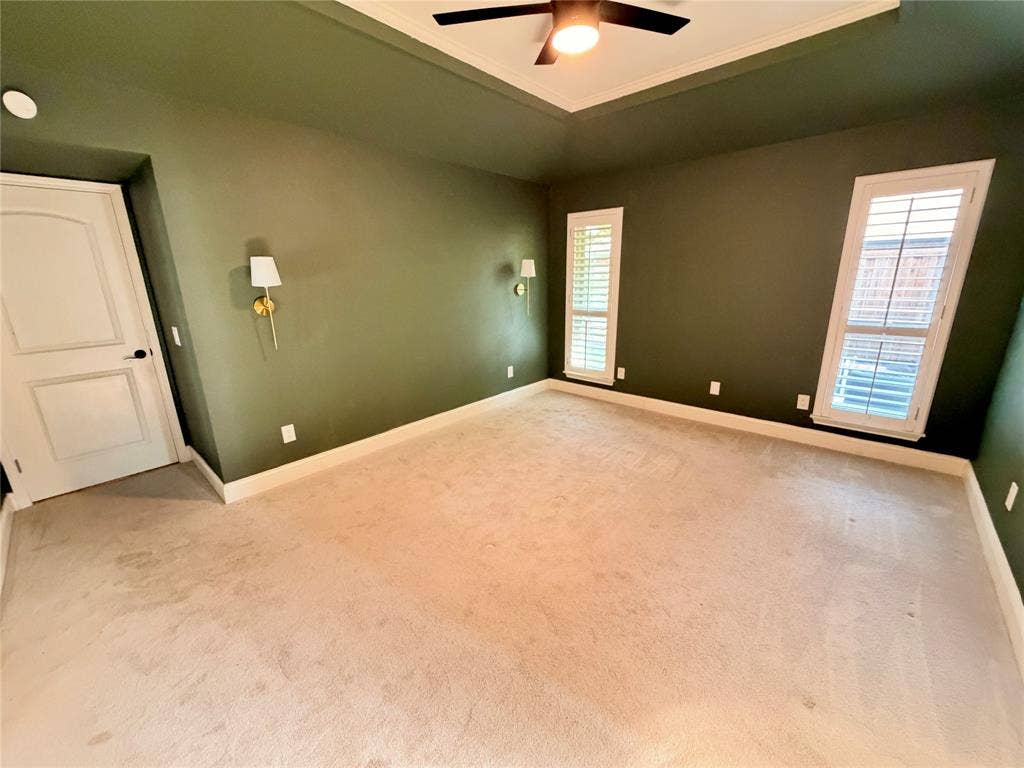 Tray ceiling featuring a central lighted ceiling fan, dual wall-mounted light fixtures, and white plantation shutters