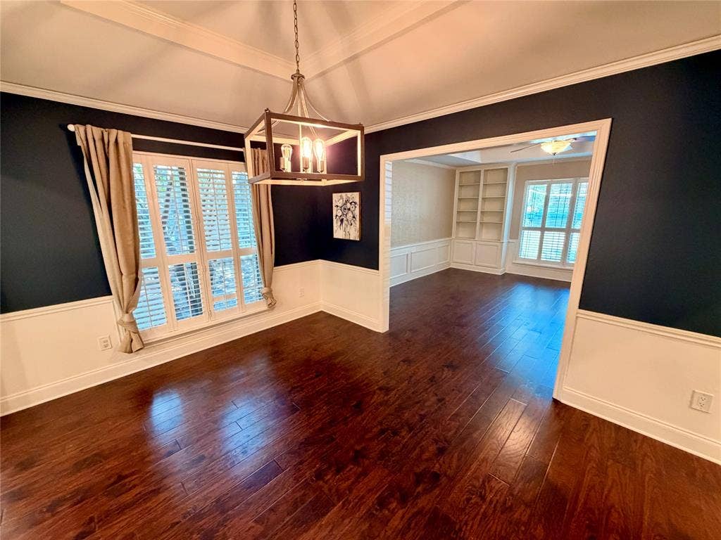 Wood-finish flooring, two-tone walls with wainscoting, tray ceiling, geometric-frame chandelier, and built-in shelving
