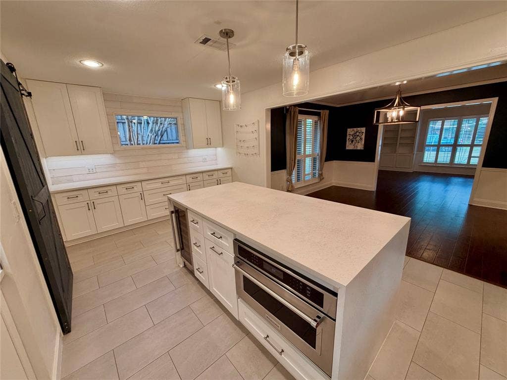 Kitchen featuring a central island with quartz countertop, light-toned cabinetry, stainless steel built-in appliances, pendant lighting, and horizontal wall paneling