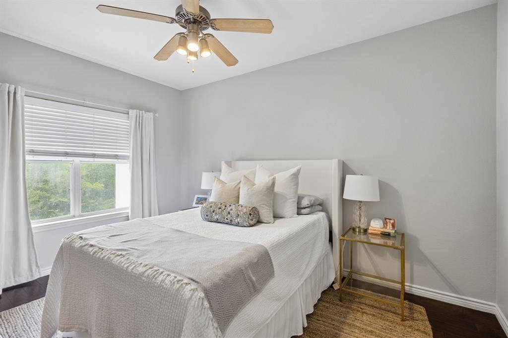 Bedroom featuring light gray walls, dark wood-finish flooring, a window with blinds, white trim, and a ceiling fan with integrated lighting