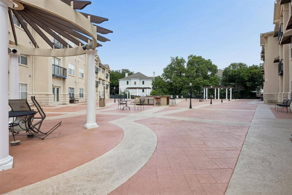 Expansive paved courtyard featuring decorative pergolas, outdoor lighting, and a built-in outdoor kitchen area