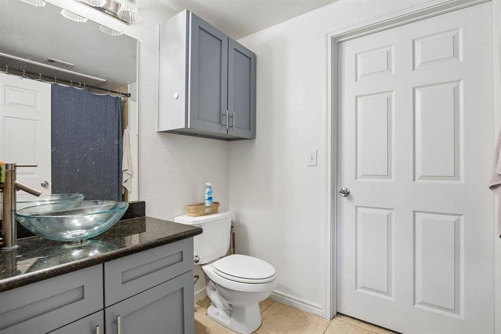 Bathroom featuring a vessel sink, dark stone-finish countertop, light gray cabinetry, and neutral tile flooring
