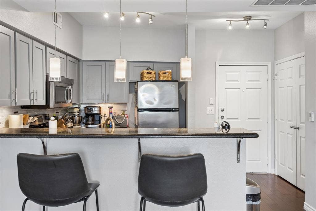 Kitchen featuring gray cabinetry, dark countertops, stainless steel appliances, and integrated bar seating