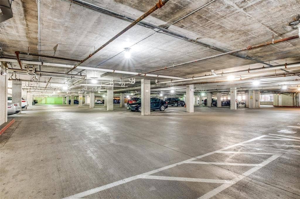 Spacious concrete parking garage with multiple columns, overhead piping, and ceiling-mounted lighting fixtures