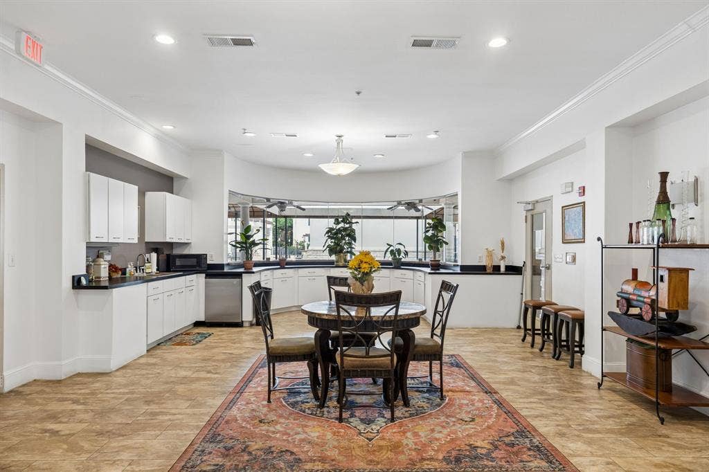 Spacious common area featuring light-toned tile flooring, recessed lighting, and a kitchen area with white cabinetry and dark countertops