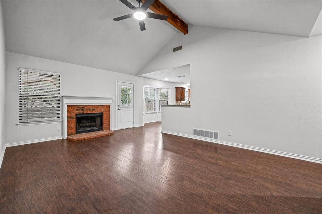 7929 Sunrise Drive, Watauga, TX 76148 Vaulted ceiling featuring a decorative wood-finish beam, wood-finish flooring, masonry fireplace with a classic mantel, and a ceiling fan with integrated lighting