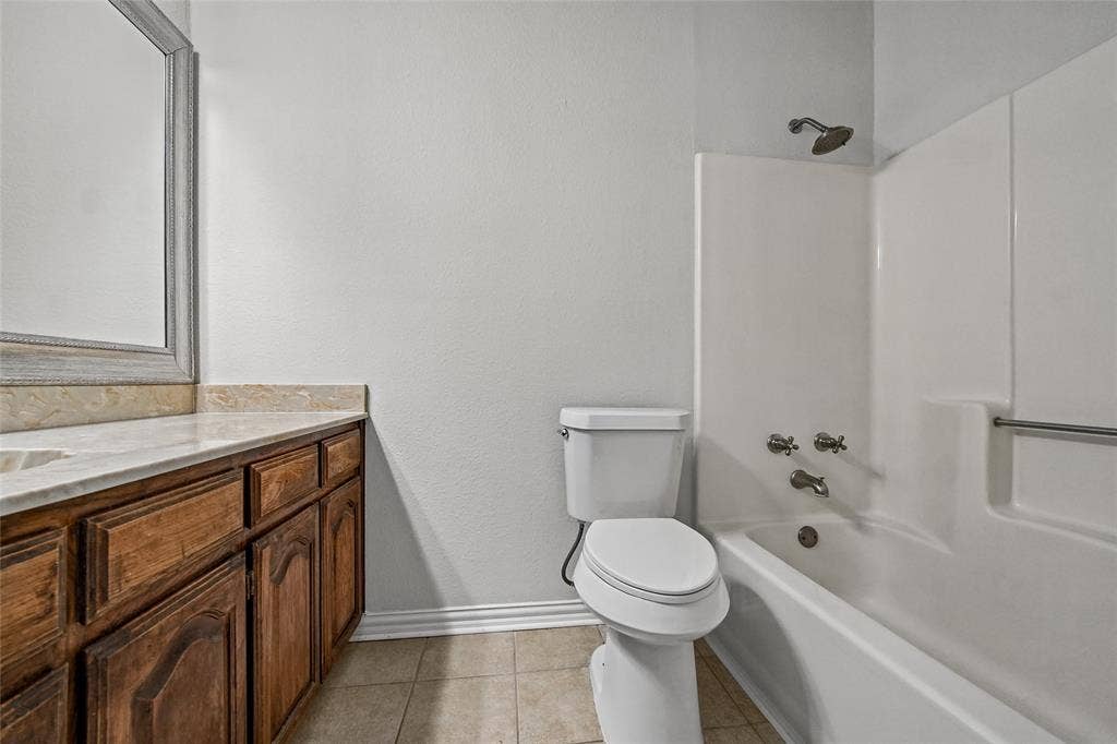 7929 Sunrise Drive, Watauga, TX 76148 Bathroom featuring a wood vanity with stone countertop, integrated sink, framed wall mirror, and a tub-shower combination with metal fixtures