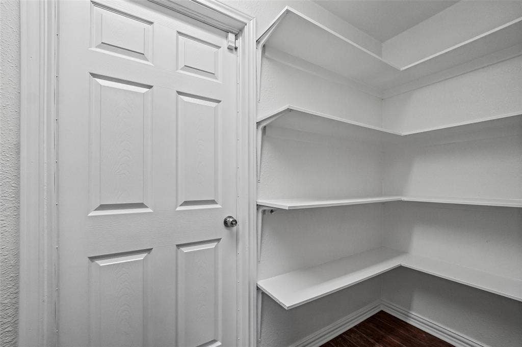 7929 Sunrise Drive, Watauga, TX 76148 Storage area featuring white paneled door with hardware and multi-level white built-in shelving over wood-finish flooring