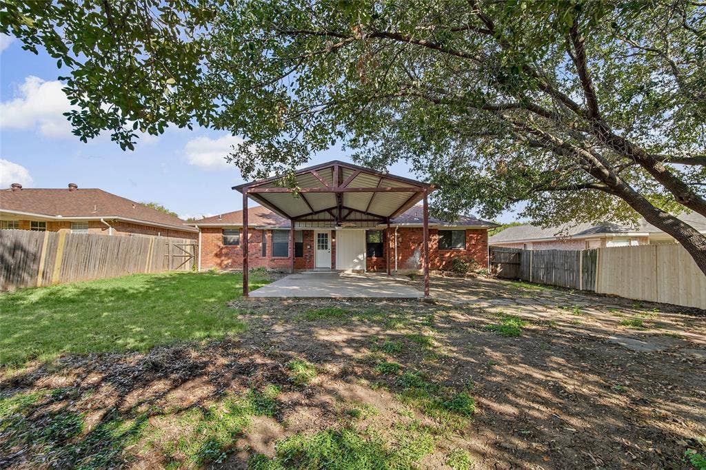 7929 Sunrise Drive, Watauga, TX 76148 Backyard featuring a covered patio with metal roofing, brick exterior, wood-style perimeter fencing, and mature trees