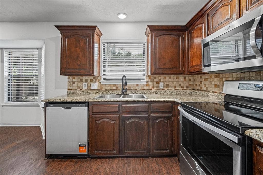 7929 Sunrise Drive, Watauga, TX 76148 Kitchen featuring stained wood cabinetry, stone-patterned countertops, a tiled backsplash, and stainless steel appliances