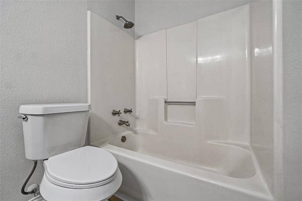 7929 Sunrise Drive, Watauga, TX 76148 Bathroom featuring a porcelain toilet and an integrated tub and shower combination with a built-in recessed storage shelf and metallic fixtures