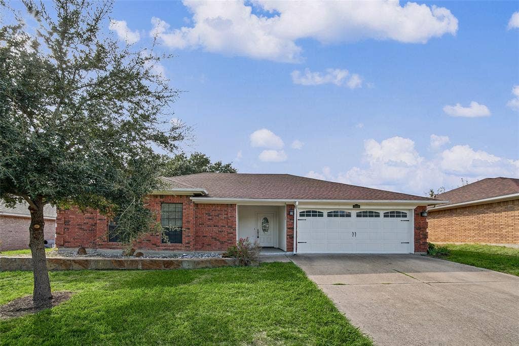 7929 Sunrise Drive, Watauga, TX 76148 Single-story brick exterior featuring an attached two-car garage, covered entryway, and stone-bordered front garden