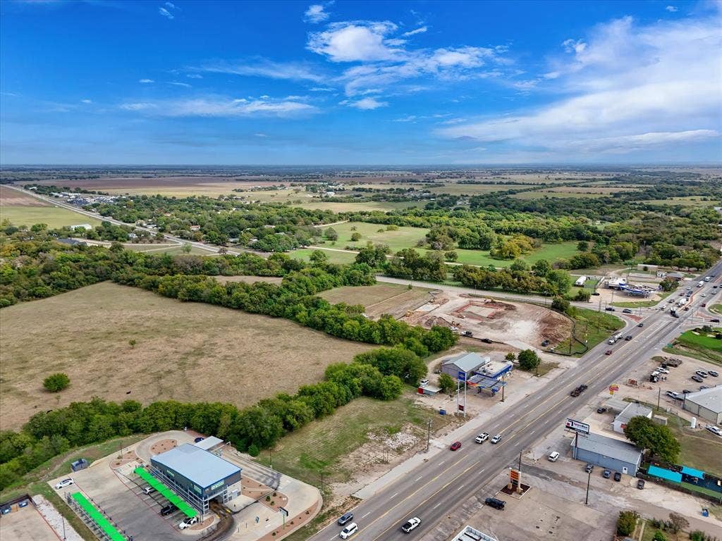 Aerial perspective featuring expansive acreage, mature tree-lined borders, and prominent frontage along a major thoroughfare