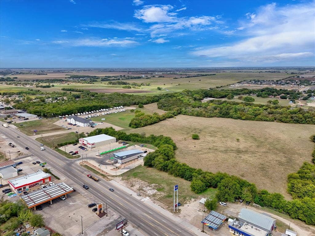 Aerial view of expansive undeveloped acreage featuring direct highway frontage, cleared terrain, and mature tree borders