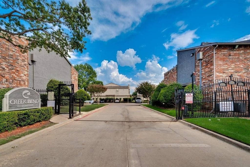 12484 Abrams Road, Dallas, TX 75243 Gated entrance featuring a concrete driveway, perimeter metal fencing, and brick-exterior structures