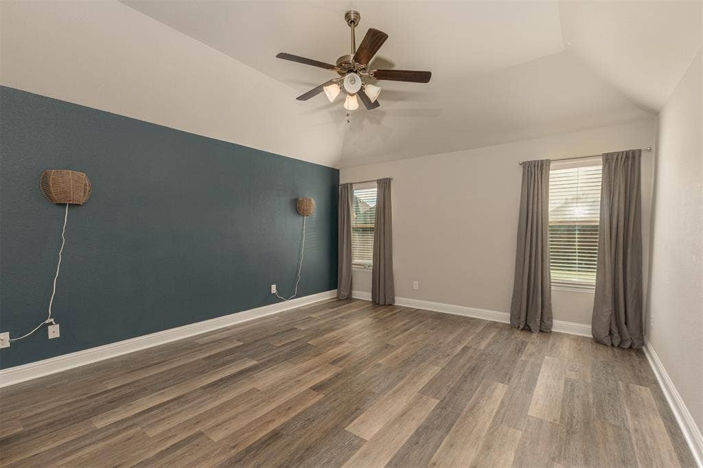 Vaulted ceiling featuring a ceiling fan with integrated lighting, wood-finish flooring, and a decorative accent wall