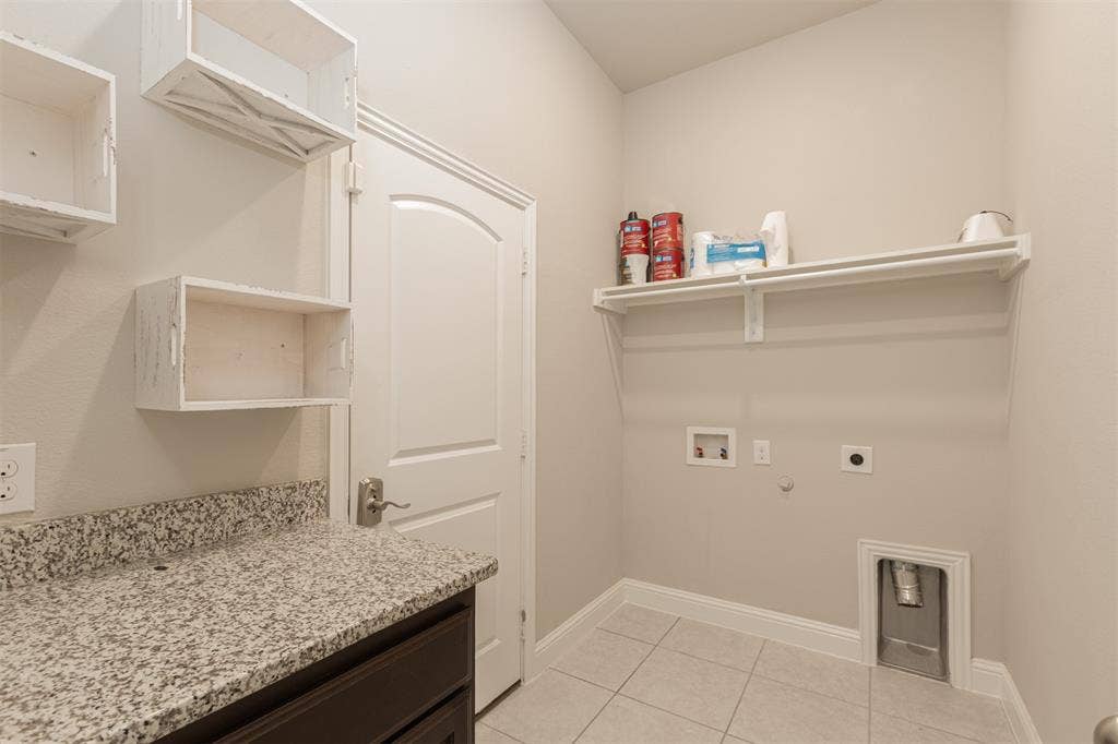 Utility room featuring stone-finish countertops, built-in cabinetry, tile flooring, and a wall-mounted shelving unit