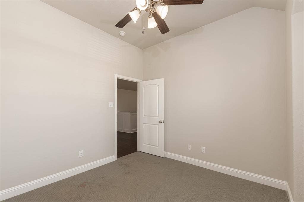 Vaulted ceilings, neutral wall tones, carpeted flooring, and a multi-blade ceiling fan with integrated lighting