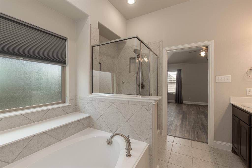 Soaking tub featuring a deck-mounted brushed nickel faucet, separate glass-enclosed shower with tiled surround, and high ceilings