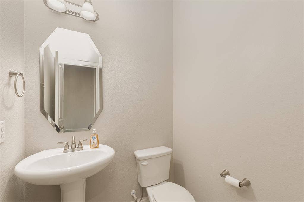 Pedestal sink featuring a polished chrome widespread faucet, octagonal wall-mounted mirror, and two-light vanity fixture