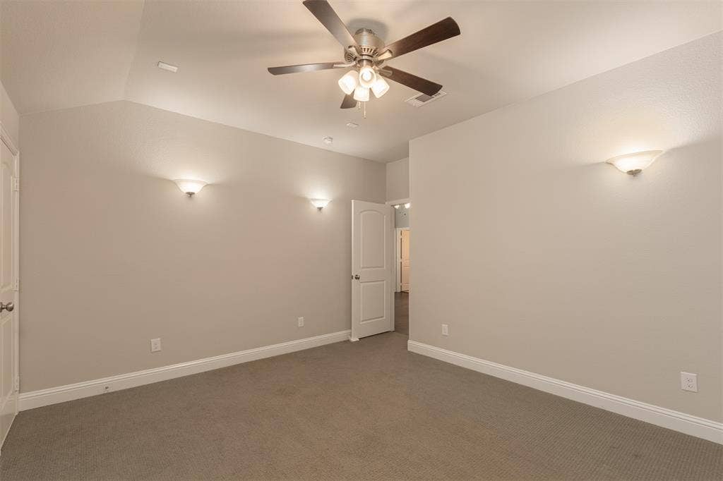 Vaulted ceiling, neutral wall tones, carpeted flooring, multi-light ceiling fan, and wall-mounted sconce lighting