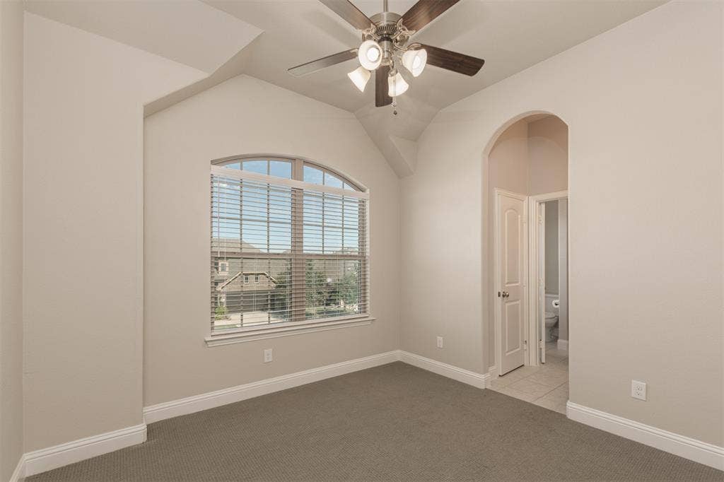 Vaulted ceilings with an arched window, neutral wall palette, ceiling fan with integrated lighting, and a prominent arched entryway