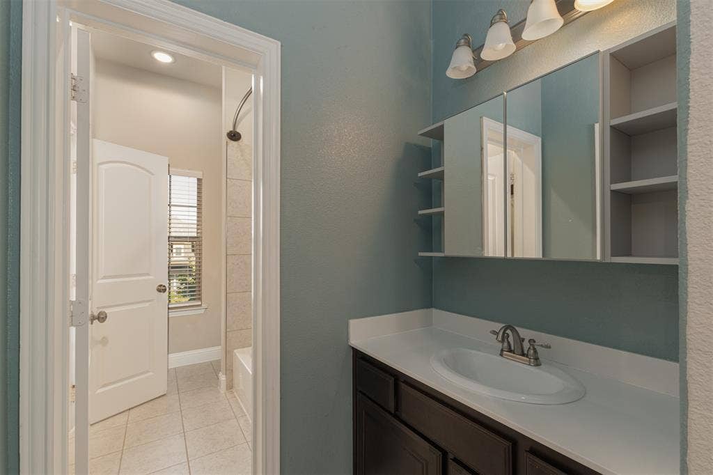 Dark wood cabinetry, white stone-composite countertop with an integrated oval sink, four-light vanity fixture, and mirrored medicine cabinet with side shelving