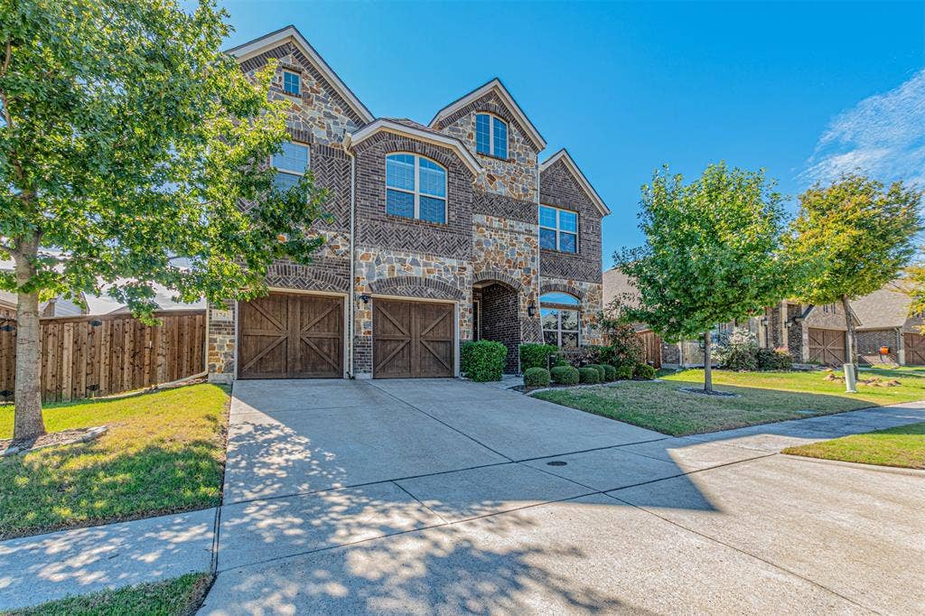 Two-story exterior featuring a stone and brick facade, arched window detailing, and dual carriage-style garage doors
