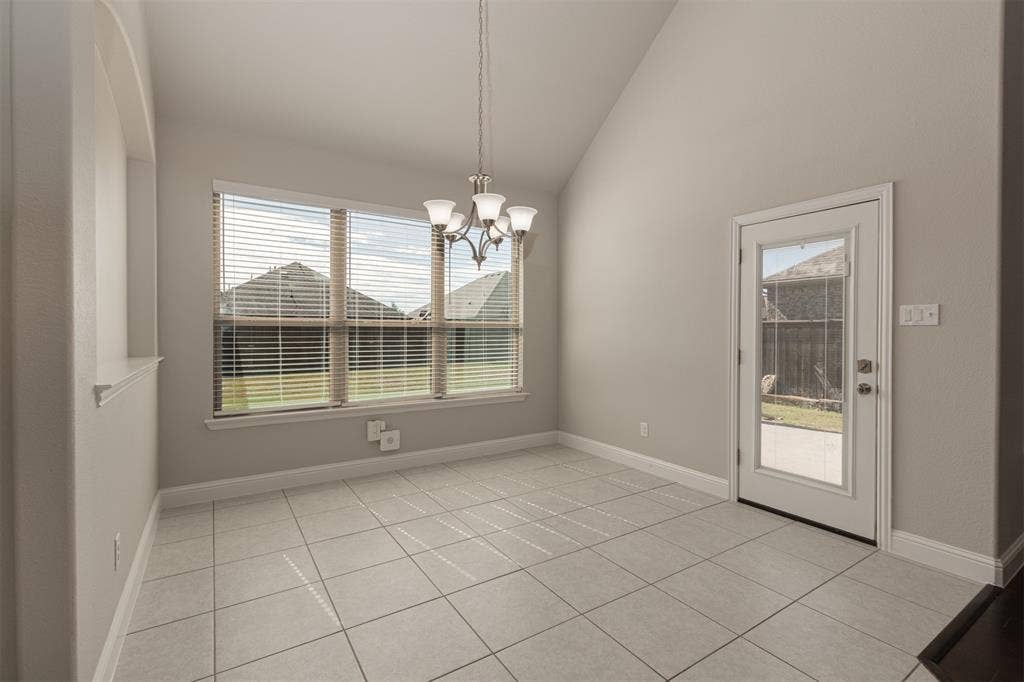 Vaulted ceilings, neutral tile flooring, multi-pane window with natural light, multi-light chandelier, and glass-paneled exterior door