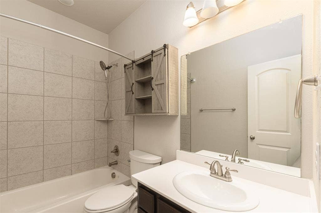 Bathroom featuring a white vanity with an integrated sink, large wall-mounted mirror, sliding barn-door style cabinetry, and a shower-tub combination with tiled surround