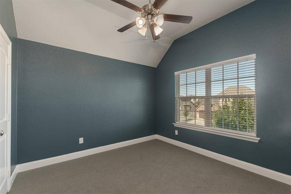 Vaulted ceiling with an integrated ceiling fan, neutral carpeting, and a large multi-pane window with horizontal blinds