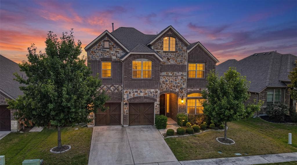 Multi-story residence featuring a stone and brick facade, dual-car garage with carriage-style doors, and an arched entryway