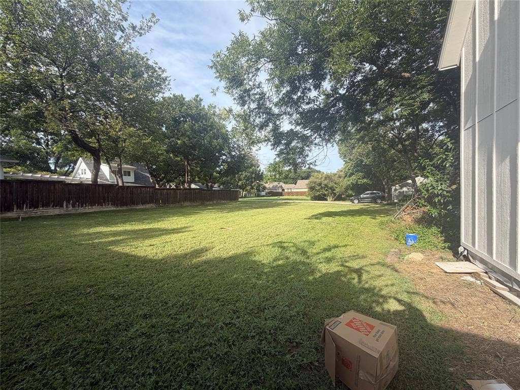 Expansive backyard featuring a large grass lawn, mature trees, and wooden perimeter fencing