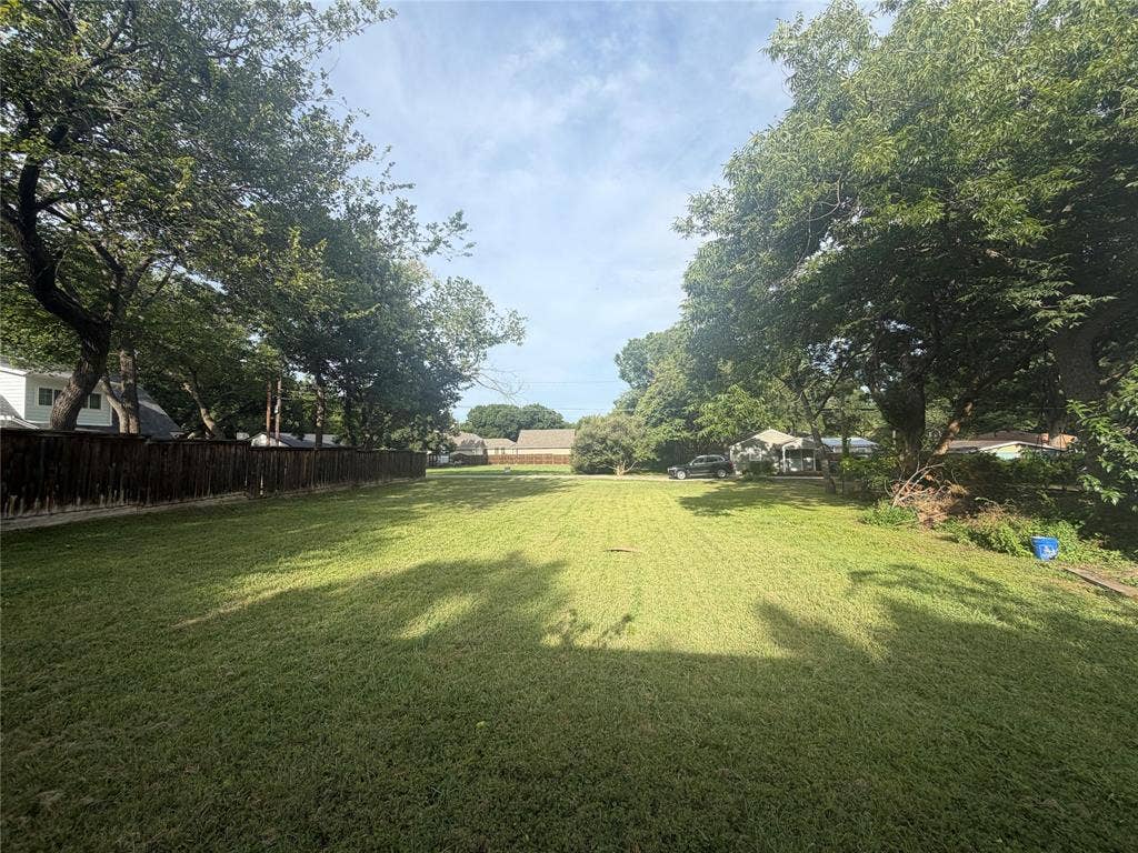 Expansive backyard featuring a large grass lawn, mature trees, and wooden perimeter fencing