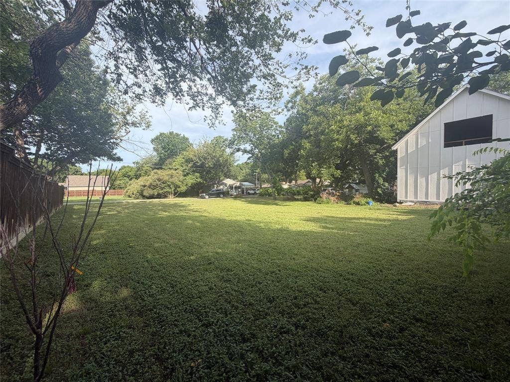 Expansive lot featuring mature trees, a wood-slat perimeter fence, and a white board-and-batten exterior structure