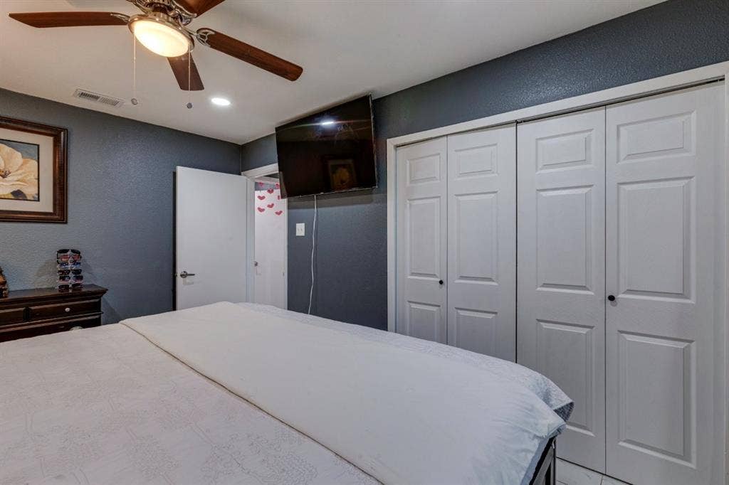 Bedroom featuring a dark-toned accent wall, a four-blade ceiling fan with an integrated light fixture, and dual-panel closet doors