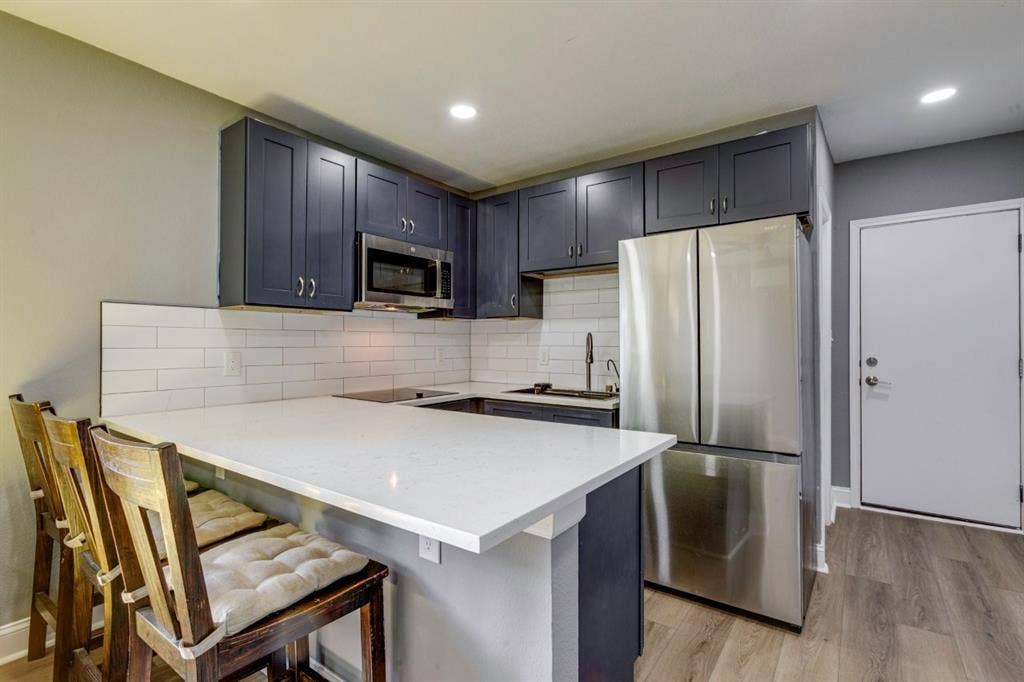 Kitchen featuring dark shaker-style cabinetry, quartz countertops with an extended breakfast bar, white subway tile backsplash, stainless steel appliances, and wood-finish flooring