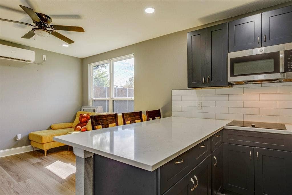 Kitchen featuring dark-finish cabinetry, quartz countertops, white subway tile backsplash, stainless steel microwave, and wood-finish flooring