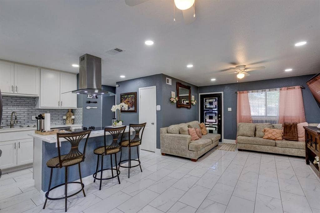 Open-concept kitchen and living area featuring white cabinetry, a stainless steel chimney-style range hood, recessed lighting, and tile flooring