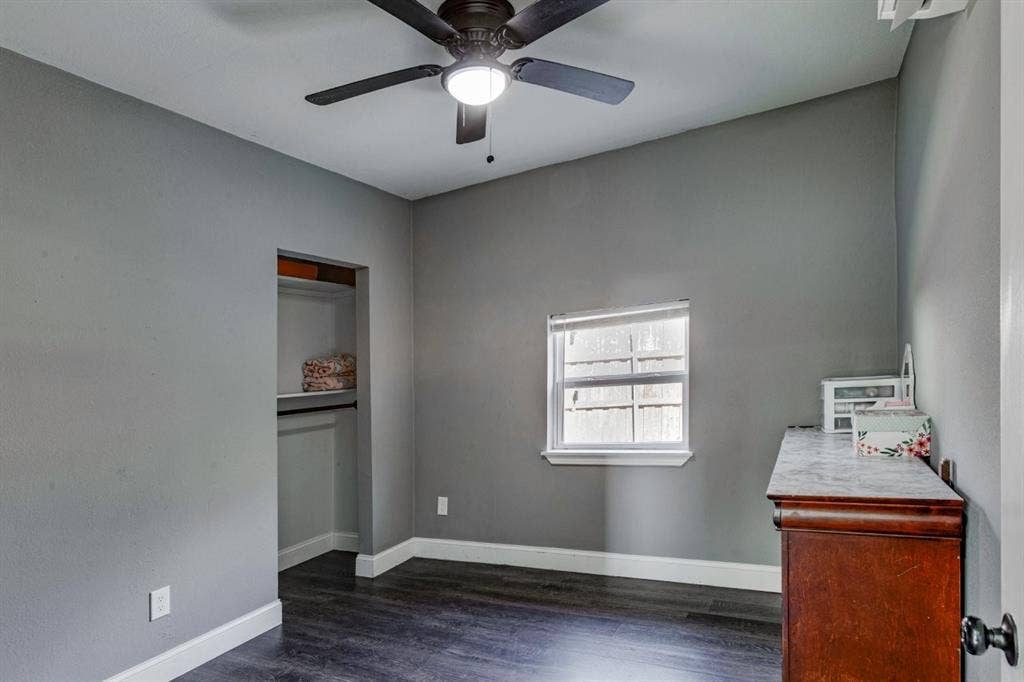 Room featuring dark wood-finish flooring, a neutral wall palette, a built-in reach-in closet, a ceiling fan with integrated lighting, and a window with a horizontal blind