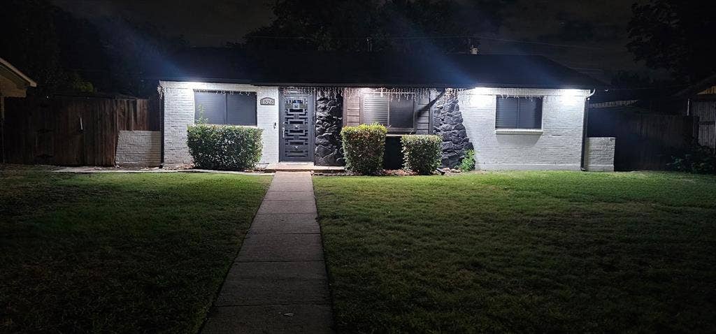 Exterior facade featuring white painted brick, decorative dark stone masonry accents, a central entry door with inset windows, and a concrete walkway