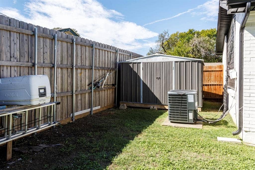 Exterior side yard featuring a wood privacy fence, a metal storage shed, and an HVAC condenser unit