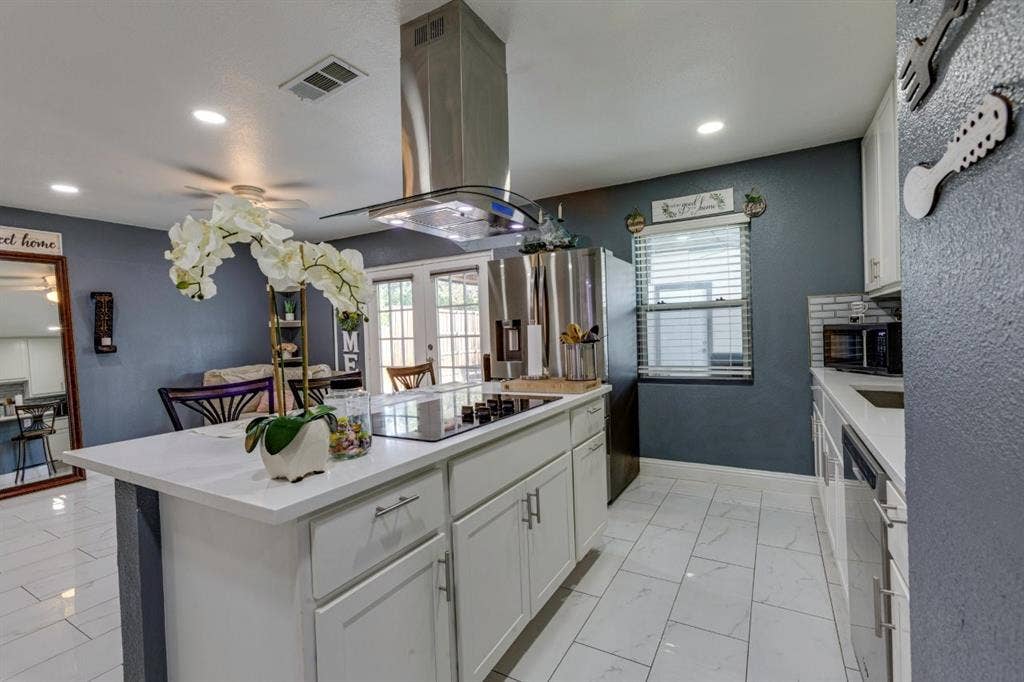 Kitchen featuring an island with a smooth-surface cooktop, stainless steel chimney-style range hood, white shaker-style cabinetry, and polished tile flooring