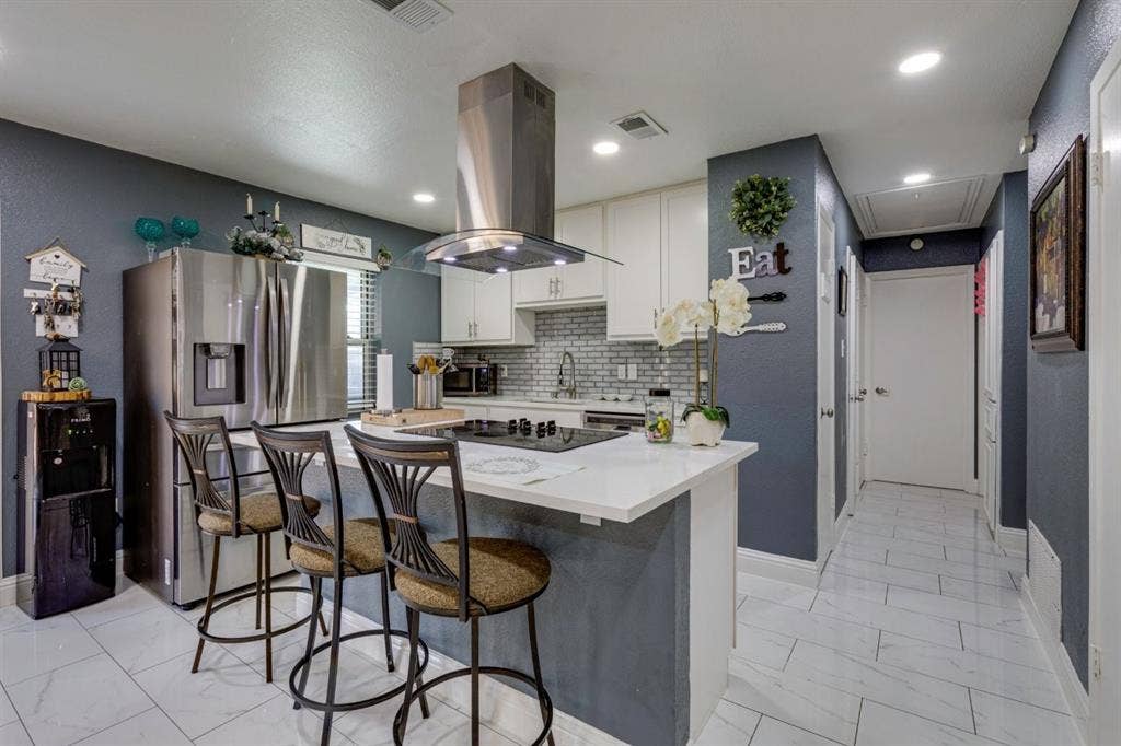 Kitchen featuring white cabinetry, solid-surface countertops, stainless steel appliances, a center island with a built-in cooktop and stainless steel range hood, and tile flooring